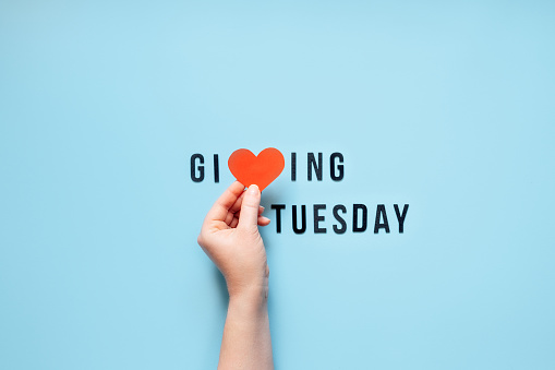 Giving Tuesday, Give, Help, Donation, Support, Volunteer concept with red heart in female hands and text Giving Tuesday on blue background. Es hora de dar photo