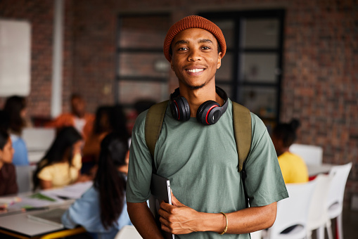 Smiling young male college student wearing headphones standing in a classroom