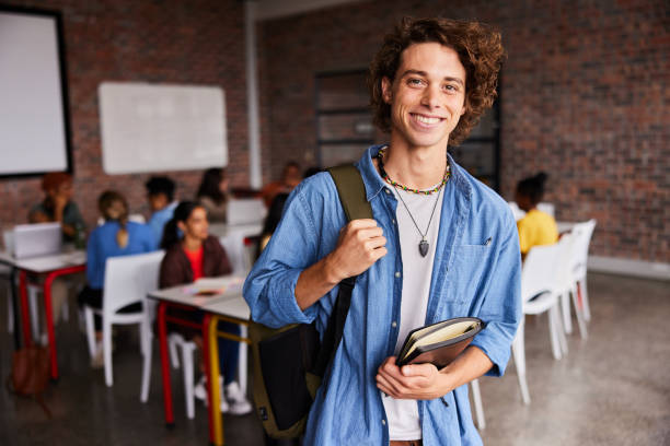 istock Young male colleage student with a backpack smiling in a classroom 1438970052