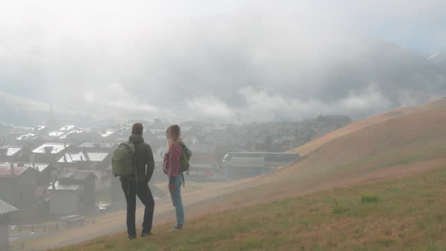 Young man and woman look down upon town from foggy hillside