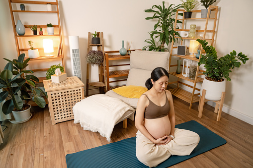 Beautiful pregnant woman sitting on exercise mat and making relaxing exercise during late pregnancy.