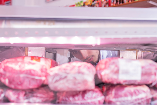 Latino butcher shop employee from Bogota Colombia between 40 and 49 years old, fills the freezer with a lot of packaged meat