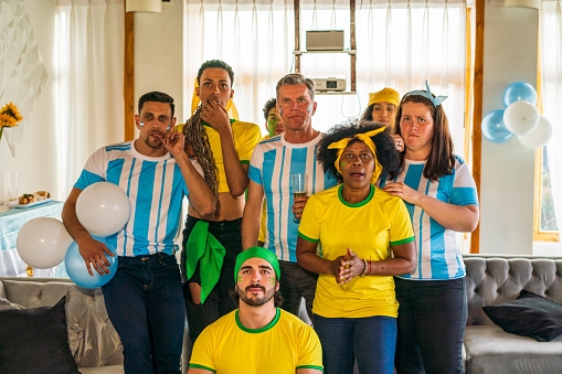 Group of people of different ages and ethnicities from the teams of Brazil and Argentina are watching the matches of the soccer world cup