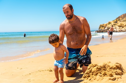 Father playing in the sand, Praia do Barranco das Belharucas beach, Albufeira, Algarve. Portugal