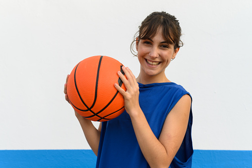 Basketball player woman with carefree smile holding basketball ball isolated on blue and white background.