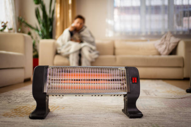 woman warming her hands over electric heater at home Person heating their hands at home over a domestic portable radiator in winter, energy crisis space heater stock pictures, royalty-free photos & images