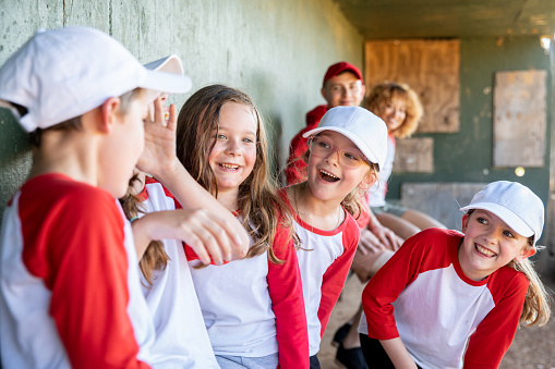 Excited group of children laugh while sitting in dugout during baseball game