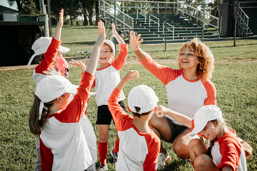 Young woman is coaching little league team and huddling with them during game