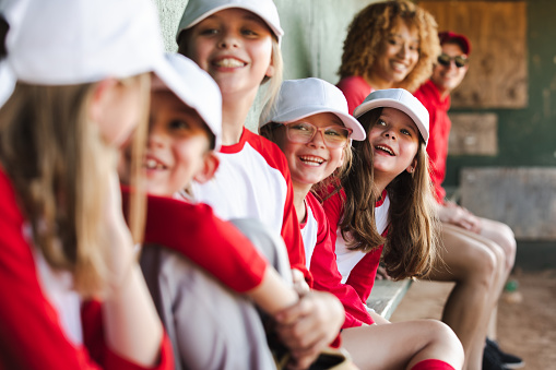 Little league team has fun together while sitting in dugout during baseball game