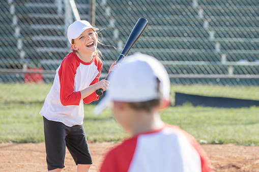 Girl laughs while up to bat during little league baseball game