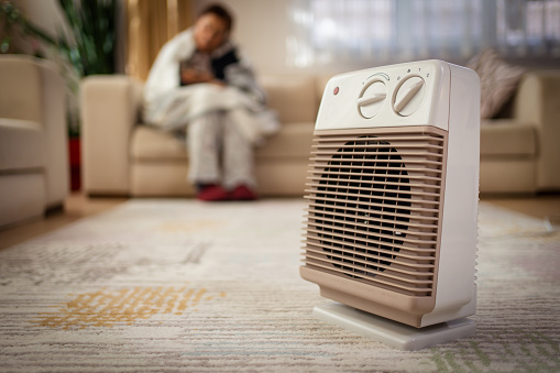 Person heating their hands at home over a domestic portable radiator in winter, energy crisis