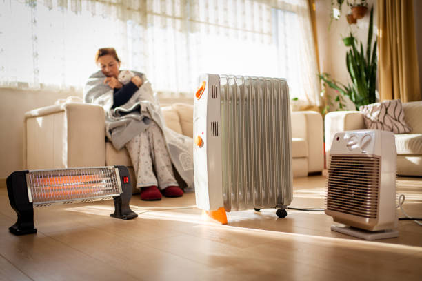 woman warming her hands over electric heater at home