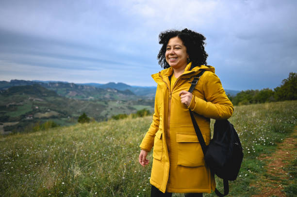 istock woman in a yellow jacket with backpack walks in the meadow. 1438987345