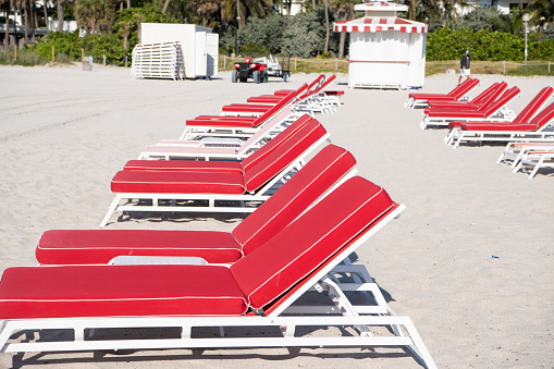 Rows of red sunchairs chaise lounges beach furniture on sand in summer.