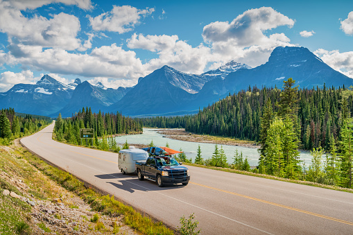 Pick-up truck with travel trailer and kayaks drives on the Icefields Parkway in Jasper National Park, Canadian Rockies.