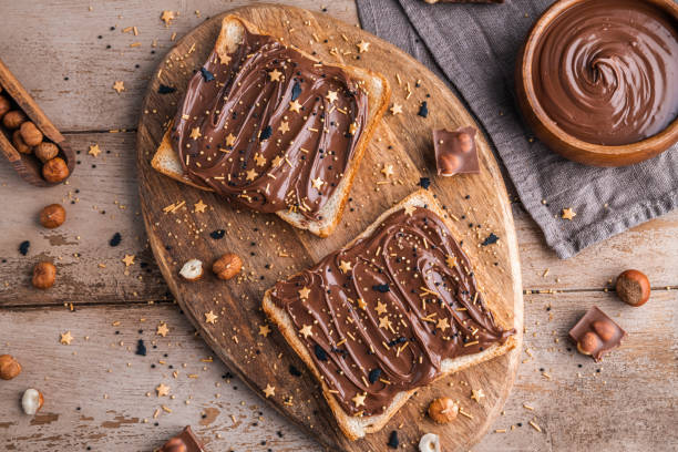 istock Board of bread with chocolate paste and hazelnuts on wooden background 1438989005