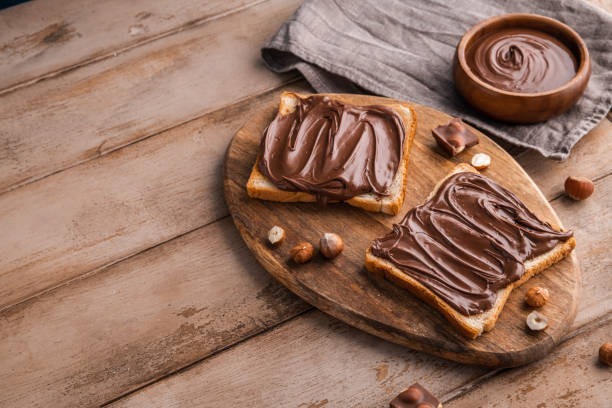 istock Board of bread with chocolate paste and hazelnuts on wooden background 1438989154