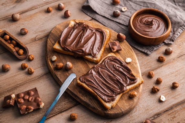 istock Board of bread with chocolate paste and hazelnuts on wooden background 1438989221