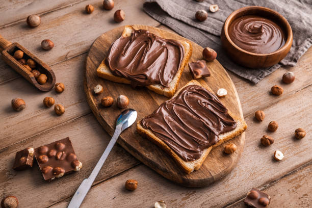 istock Board of bread with chocolate paste and hazelnuts on wooden background 1438989230
