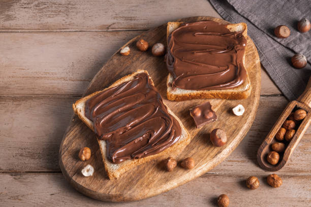 istock Board of bread with chocolate paste and hazelnuts on wooden background 1438989259