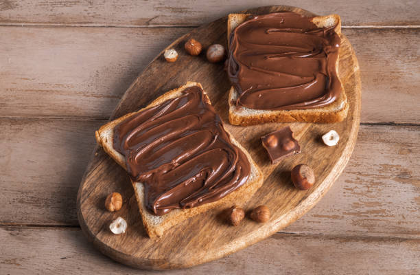 istock Board of bread with chocolate paste and hazelnuts on wooden background 1438989299