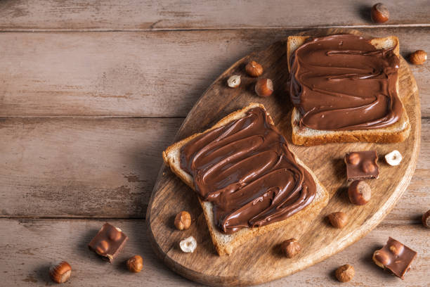 istock Board of bread with chocolate paste and hazelnuts on wooden background 1438989321