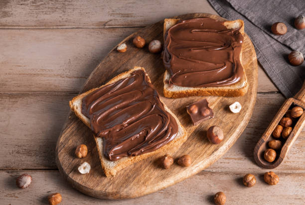istock Board of bread with chocolate paste and hazelnuts on wooden background 1438989327