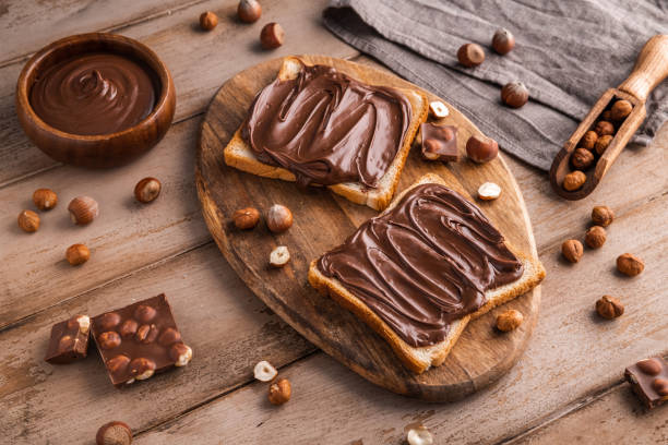 istock Board of bread with chocolate paste and hazelnuts on wooden background 1438989335