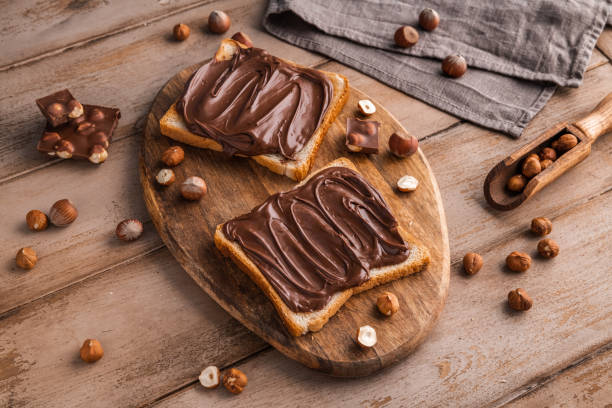 istock Board of bread with chocolate paste and hazelnuts on wooden background 1438989348