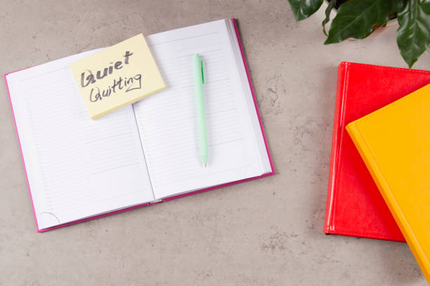 istock Workplace desk with paper business notebook planner with sticky note and text Quiet Quitting on it. Work-to-rule, in which employees engage in work related activities solely within defined work hours 1438993006