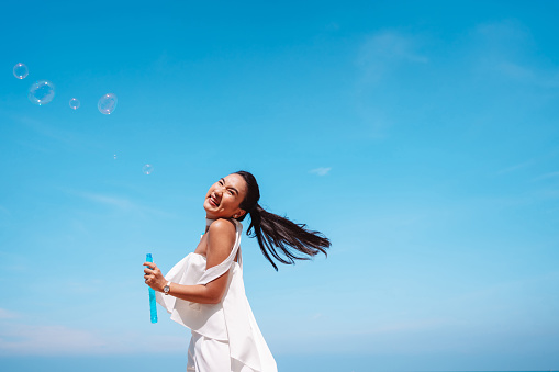 Happy beautiful young asian woman blowing soap bubbles feeling having fun enjoy on the beach outdoors.