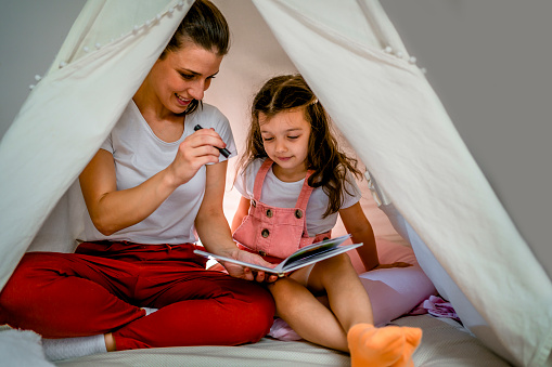 Mother reading a story to her daughter in the tent at home