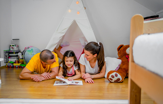 Young family lying on the floor and reading book together at home