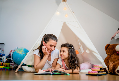 Mother and daughter reading book together in children's tent at home