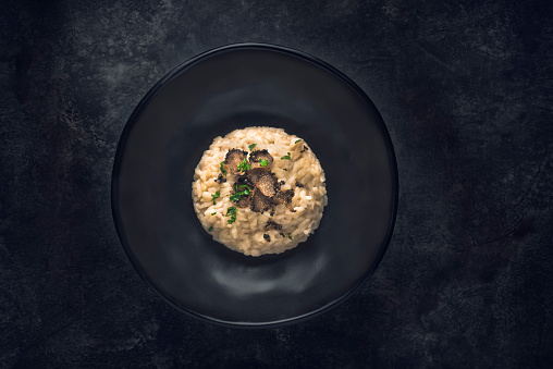 Black truffle risotto recipe.  Autumn creamy consistency risotto in stylish black dish on the black background. Dark autumn or winter mood in the style of the Chef's table
