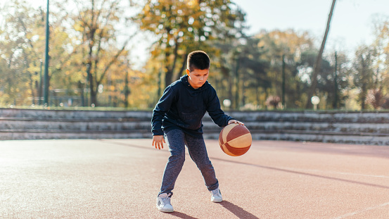 Boy playing basketball alone outdoors. He has a lot of fun. Beautiful sunny day, nice court