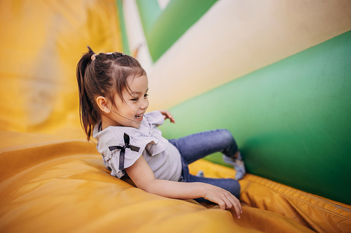 Cute little girl playing in inflatable bouncy castle in amusement park.