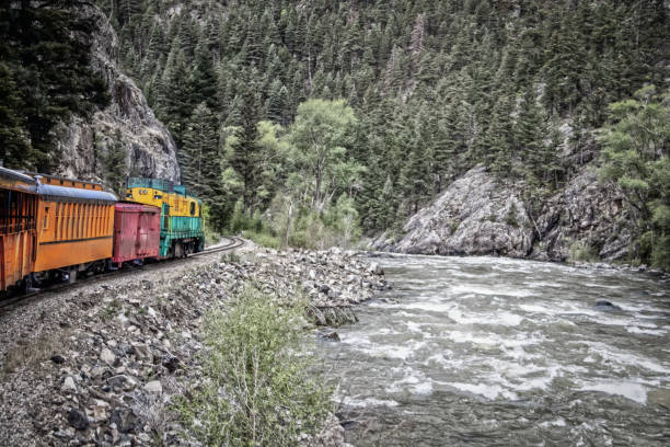 istock Steam engine rounding a curve with mountain cliff on one side and rushing river on other in pine forested mountains - Vintage filter 1439014871