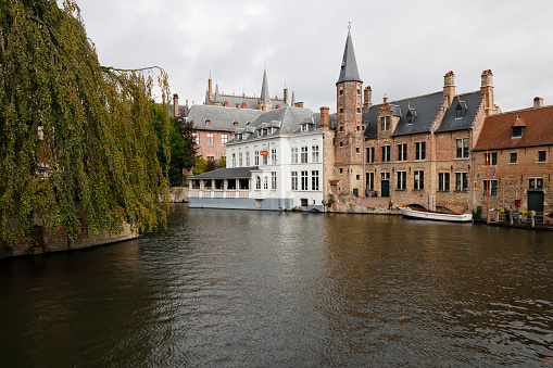 Bruges, Belgium - September 9, 2022: Brick medieval buildings on the bank of the canal bend. You can see a large tree on the edge of the canal