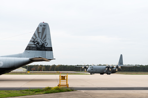 A Lockheed C-130 Hercules of the Royal Netherlands Air Force rolling onto a platform at the Dutch Air Force Base Eindhoven. On the left side of the image there is a C-130 with a special tail decoration celebrating 25 years of service.