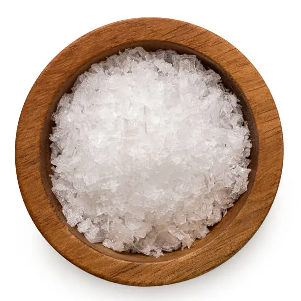 Sea salt flakes in a wood bowl isolated on white. Top view.