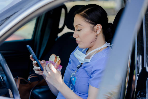 istock Female nurse uses phone while eating sandwich in car 1439023305
