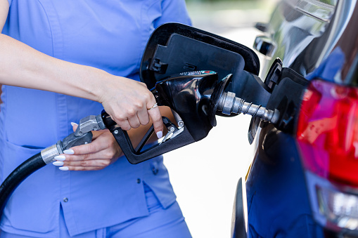 An unrecognizable healthcare professional pumps gas into the tank of her car.