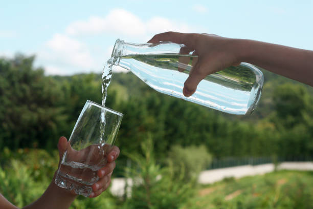 Drinking water pouring from bottle into glass on blurred green nature background