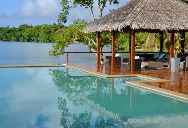 Luxury resort swimming pool in Vanuatu with thatched cabana on the pool deck and tropical beach and lagoon in the background stock photo
