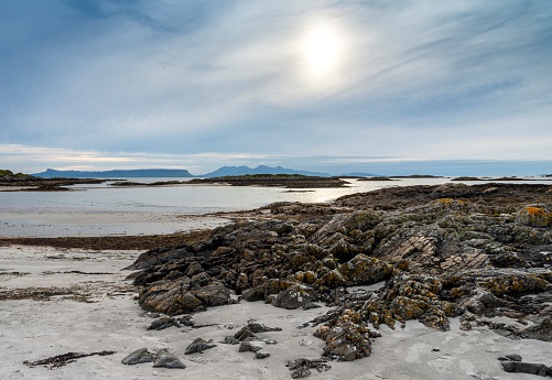 Beautiful remote,deserted beach with white sands,in mid summer,on the west coast of Scotland,at edge of Scottish Highlands,clear,calm sea,white cottages in the distance,at dusk,rugged rocks at low tide.