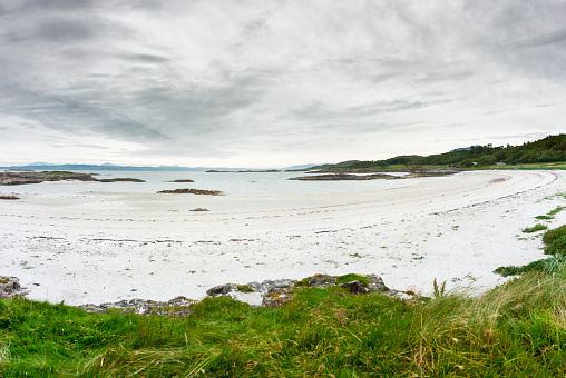 Beautiful remote,deserted beach with white sands,in mid summer,on the west coast of Scotland,at edge of Scottish Highlands,clear,calm sea,white cottages in the distance,at dusk,rugged rocks at low tide.