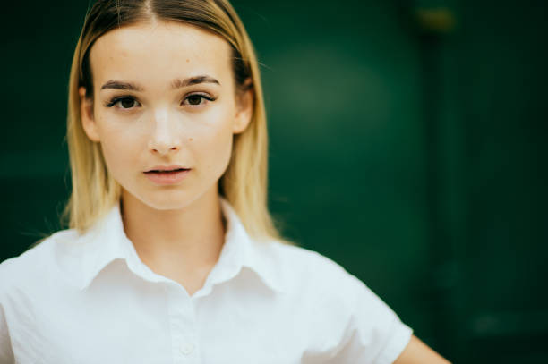 Portrait head and shoulders shot of cute young blond woman in sleeveless top looking away, studio shot.