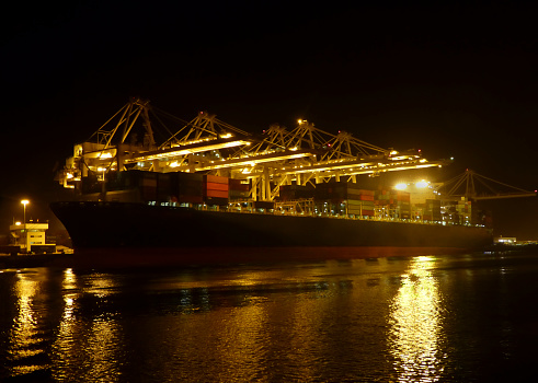 Container ships are among the largest seagoing vessels in the world.  Pictured here a massive cargo vessel is docked at night in Long Beach Harbor, California.