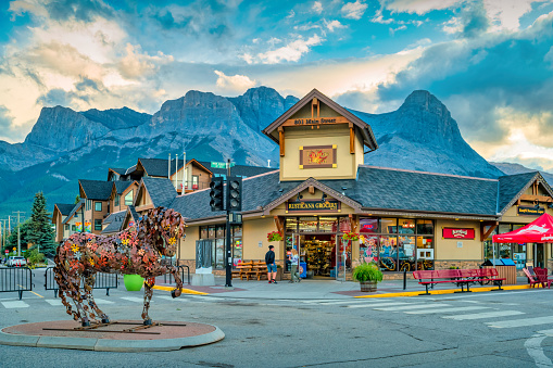 People walk past a grocery store on Main Street in Canmore, Alberta, Canada at sunset, with a horse sculpture by Cedar Mueller in the foreground.